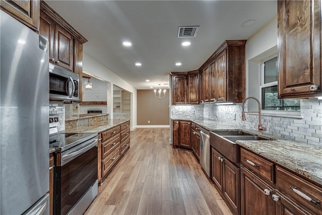 kitchen with sink, stainless steel appliances, light stone counters, backsplash, and light wood-type flooring