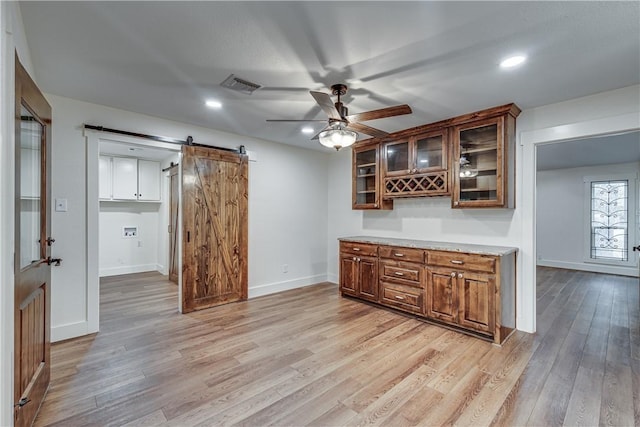 bar featuring a barn door, light hardwood / wood-style floors, and ceiling fan