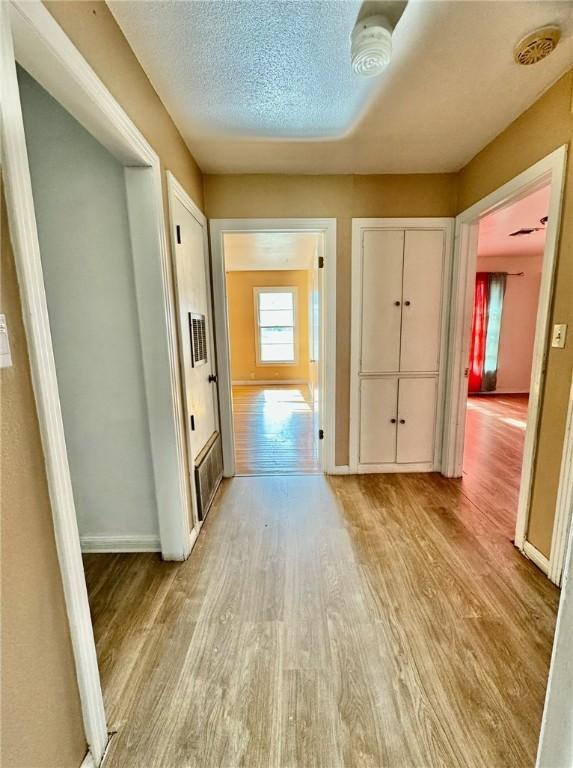 hall with light hardwood / wood-style floors and a textured ceiling