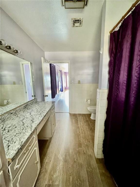 bathroom featuring vanity, wood-type flooring, tile walls, and toilet