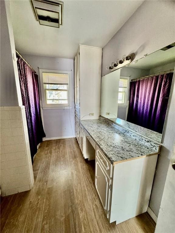 kitchen featuring white cabinets, light wood-type flooring, light stone countertops, and a healthy amount of sunlight