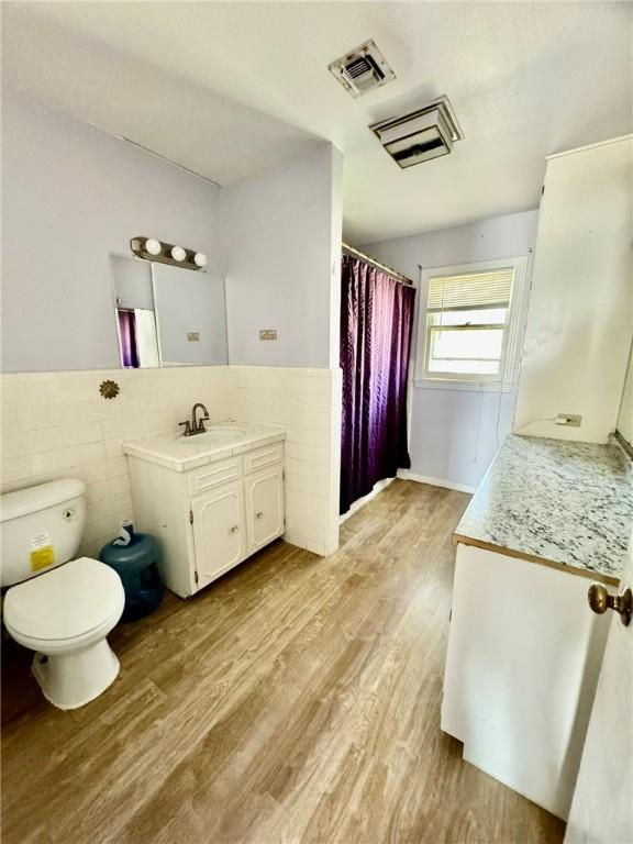 bathroom featuring wood-type flooring, vanity, toilet, and tile walls