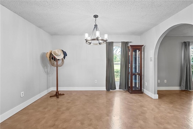 empty room with concrete flooring, a textured ceiling, and an inviting chandelier