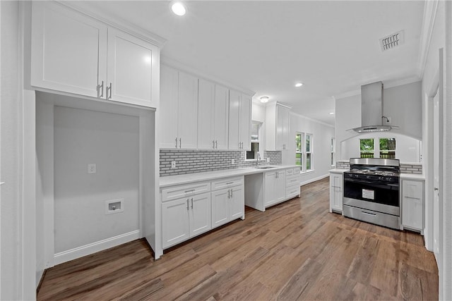 kitchen with white cabinetry, sink, ornamental molding, gas stove, and wall chimney range hood