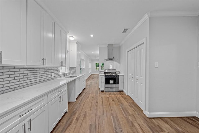 kitchen featuring wall chimney exhaust hood, sink, gas range, light stone counters, and white cabinets