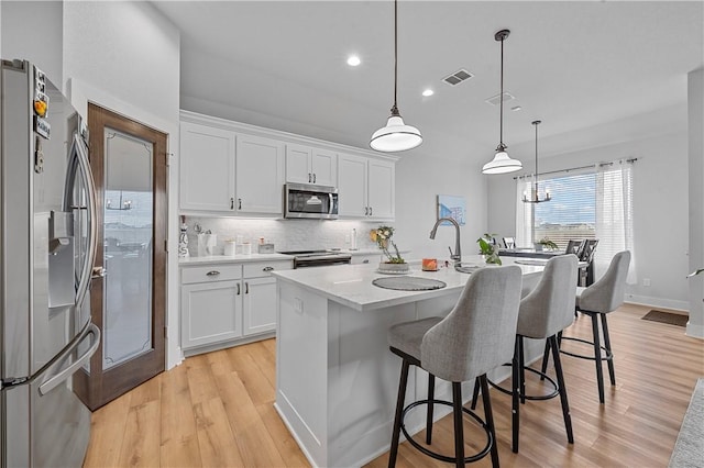 kitchen with a center island with sink, hanging light fixtures, light wood-type flooring, appliances with stainless steel finishes, and white cabinetry