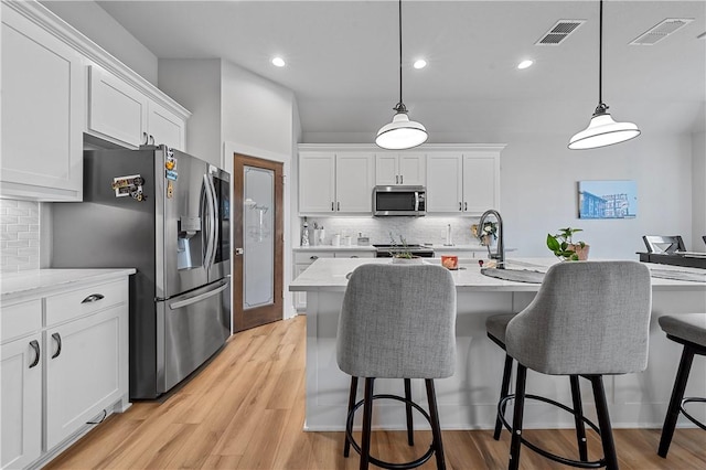 kitchen featuring white cabinets, decorative light fixtures, stainless steel appliances, and light hardwood / wood-style flooring