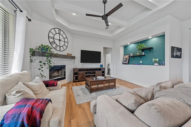 living room with hardwood / wood-style floors, ceiling fan, beam ceiling, and a tiled fireplace