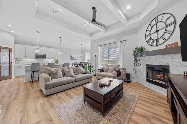 living room featuring a tray ceiling, ceiling fan, a fireplace, and light hardwood / wood-style floors