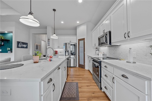 kitchen with light wood-type flooring, an island with sink, decorative light fixtures, white cabinetry, and stainless steel appliances