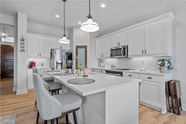 kitchen featuring white cabinets, pendant lighting, a center island with sink, and appliances with stainless steel finishes