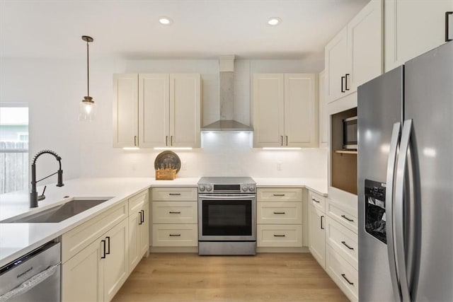 kitchen with wall chimney exhaust hood, stainless steel appliances, sink, pendant lighting, and light hardwood / wood-style flooring