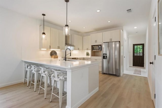 kitchen with wall chimney exhaust hood, sink, white cabinets, and appliances with stainless steel finishes