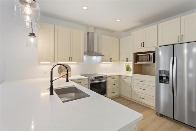 kitchen featuring sink, hanging light fixtures, wall chimney exhaust hood, light wood-type flooring, and stainless steel appliances