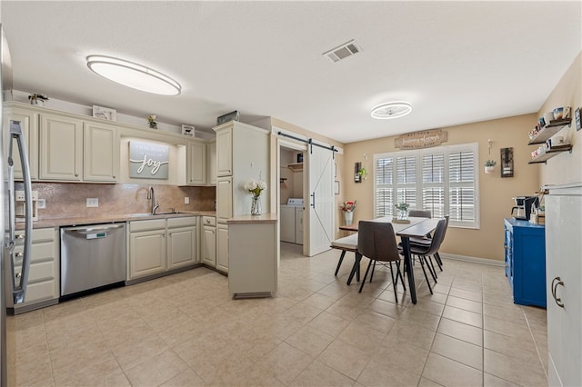 kitchen featuring visible vents, backsplash, dishwasher, a barn door, and a sink