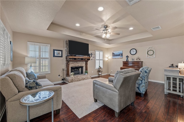 living area featuring dark wood-style floors, visible vents, a ceiling fan, and a tray ceiling