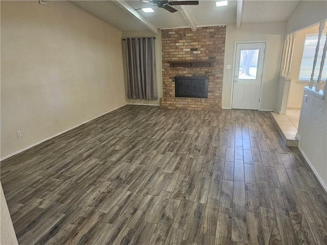 unfurnished living room with dark wood-type flooring, a brick fireplace, lofted ceiling with beams, and a ceiling fan