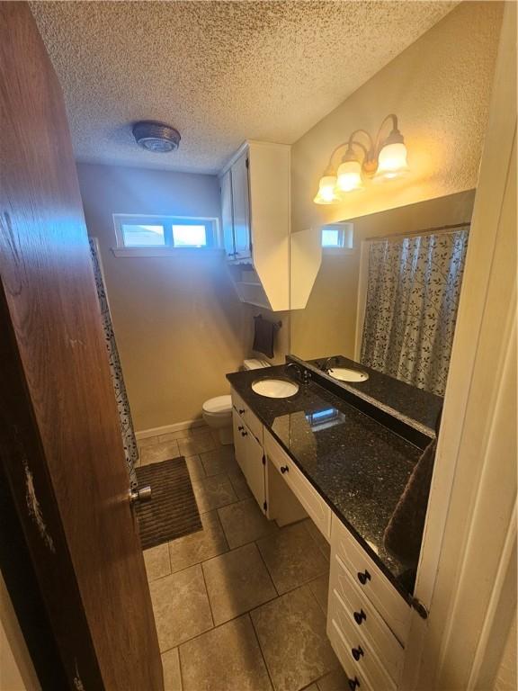 full bathroom featuring a textured ceiling, toilet, vanity, baseboards, and a shower with curtain