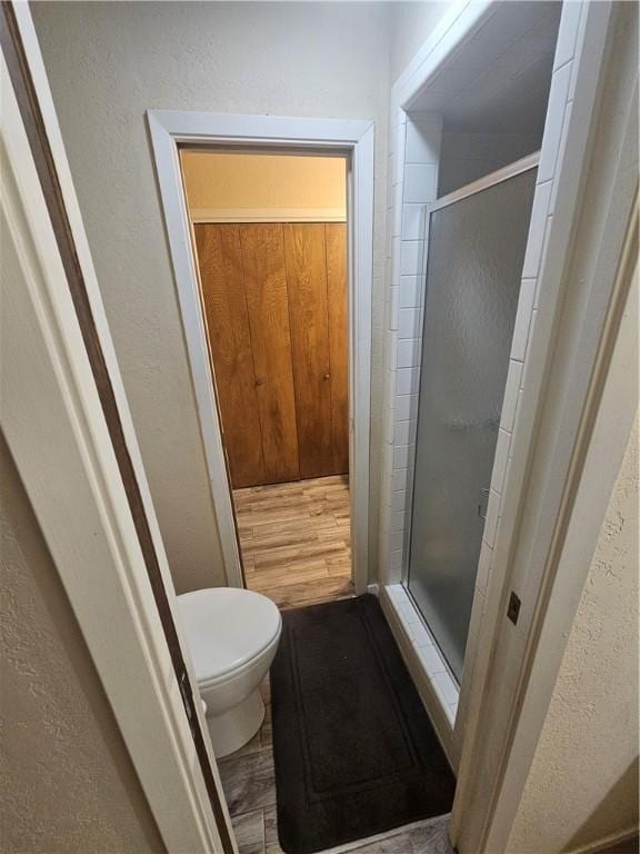 bathroom with a textured wall, a stall shower, and toilet