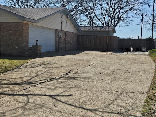 view of side of home featuring a garage, brick siding, driveway, and fence