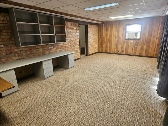 unfurnished office with a paneled ceiling, brick wall, wooden walls, and baseboards