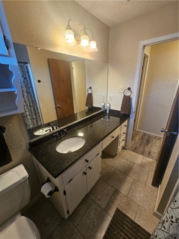 full bathroom with toilet, a textured wall, a textured ceiling, and vanity