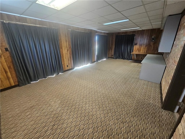 basement with wood walls, carpet flooring, and a paneled ceiling