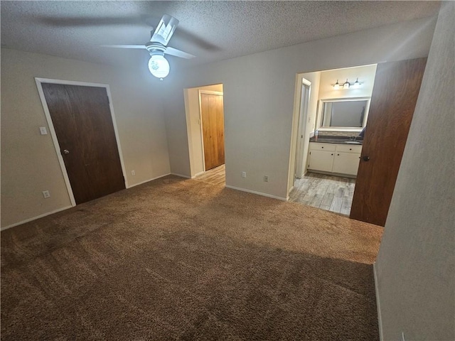 unfurnished bedroom with ceiling fan, a textured ceiling, connected bathroom, light carpet, and baseboards