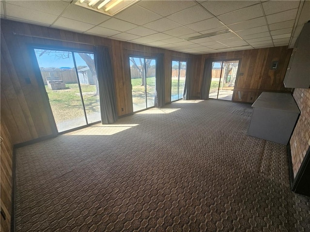 carpeted spare room featuring a drop ceiling, plenty of natural light, and wooden walls