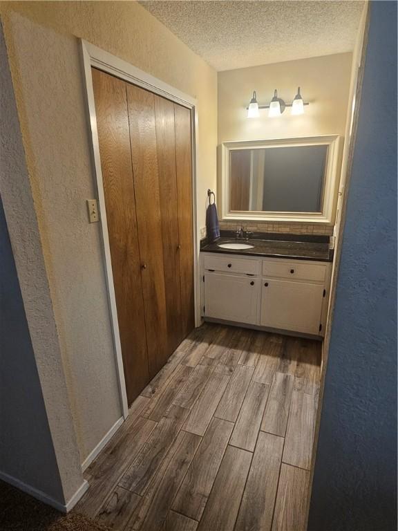 bathroom featuring a textured ceiling, vanity, wood finished floors, and a textured wall