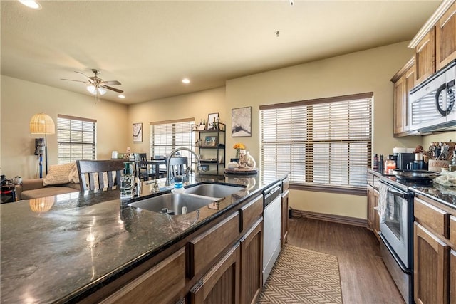 kitchen featuring appliances with stainless steel finishes, sink, dark stone countertops, dark hardwood / wood-style flooring, and ceiling fan