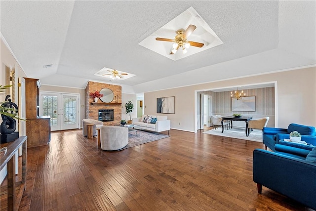 living room with a textured ceiling, hardwood / wood-style flooring, ceiling fan with notable chandelier, a fireplace, and french doors