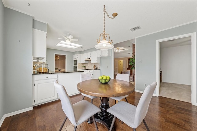 dining room featuring a skylight, baseboards, visible vents, a ceiling fan, and dark wood-type flooring