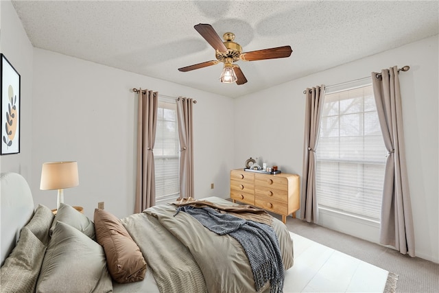 bedroom with a ceiling fan, light colored carpet, and a textured ceiling