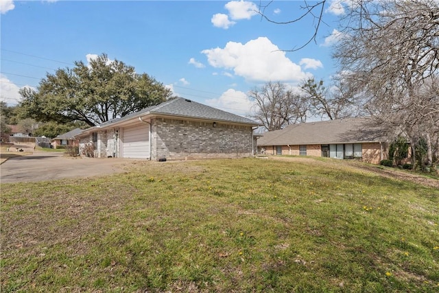 view of property exterior featuring brick siding, a yard, driveway, and an attached garage