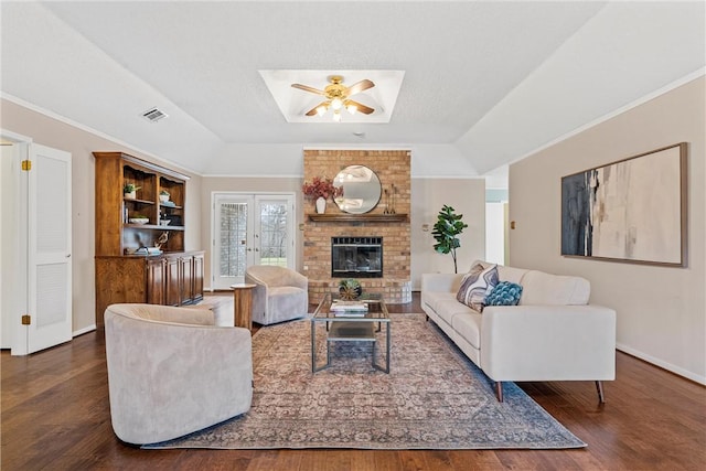 living room with a tray ceiling, visible vents, a brick fireplace, wood finished floors, and baseboards