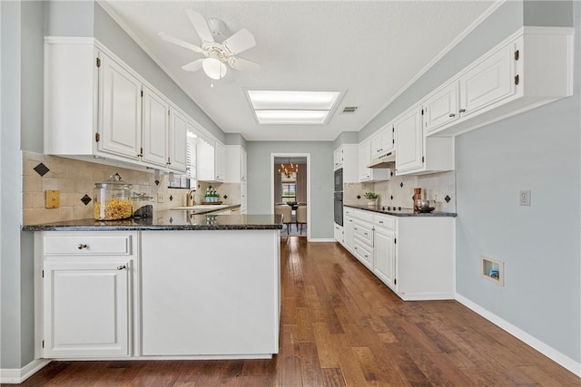 kitchen with white cabinets, dark wood-style flooring, a peninsula, under cabinet range hood, and a sink