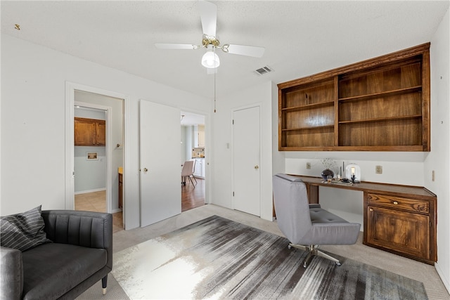 office area featuring ceiling fan, visible vents, built in desk, and light colored carpet