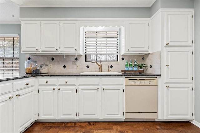 kitchen featuring dark stone countertops, white cabinetry, white dishwasher, and a sink