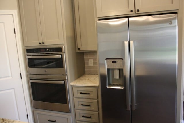 kitchen featuring backsplash, light stone countertops, white cabinetry, and appliances with stainless steel finishes