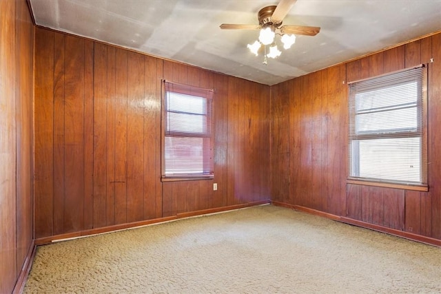 spare room featuring light carpet, ceiling fan, and wood walls