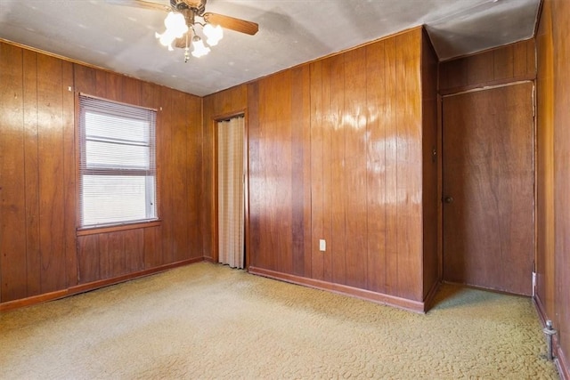 carpeted empty room with ceiling fan and wood walls