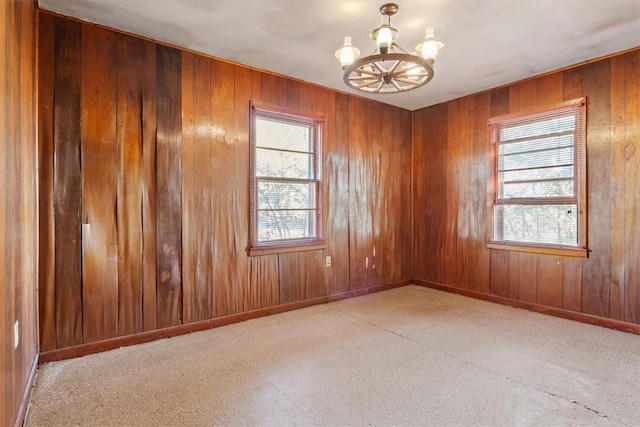 unfurnished room with wood walls and a notable chandelier