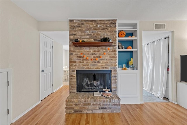 living room featuring hardwood / wood-style flooring, built in shelves, and a brick fireplace