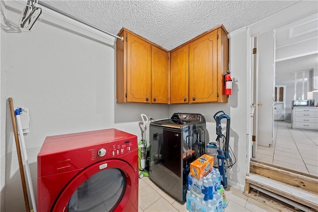 clothes washing area featuring light tile patterned floors, cabinets, a textured ceiling, and independent washer and dryer