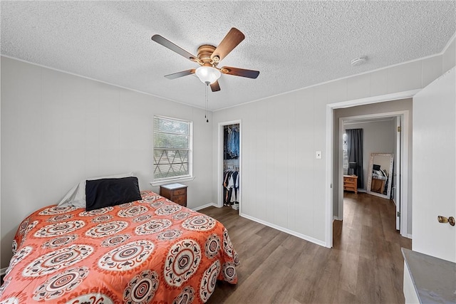 bedroom with a walk in closet, ceiling fan, a textured ceiling, wood-type flooring, and a closet