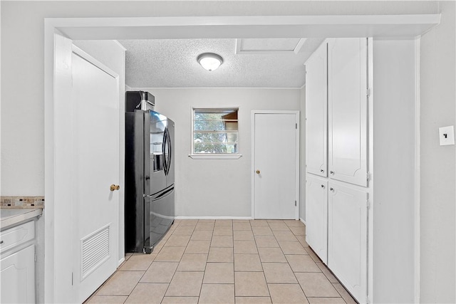 kitchen with white cabinets, stainless steel fridge, a textured ceiling, and light tile patterned flooring