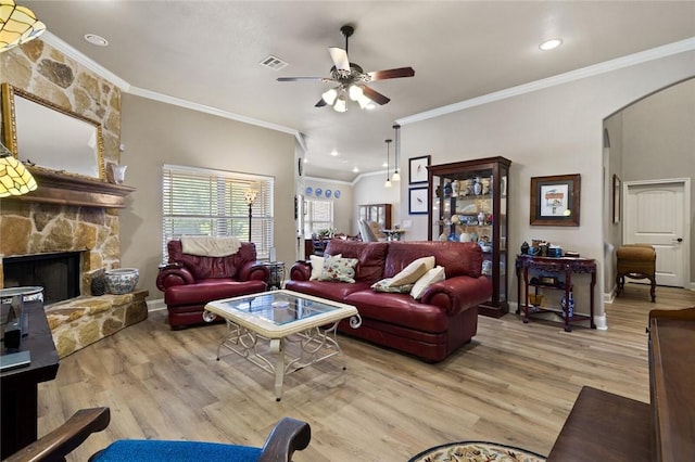 living room featuring light wood-style floors, arched walkways, a fireplace, and ceiling fan