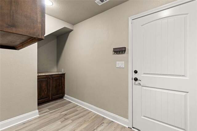 clothes washing area with arched walkways, beverage cooler, stacked washer / dryer, light wood-style floors, and cabinet space