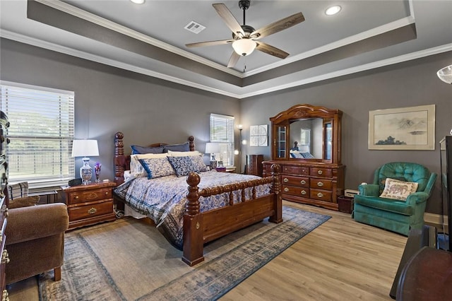 bedroom with wood finished floors, a raised ceiling, visible vents, and crown molding